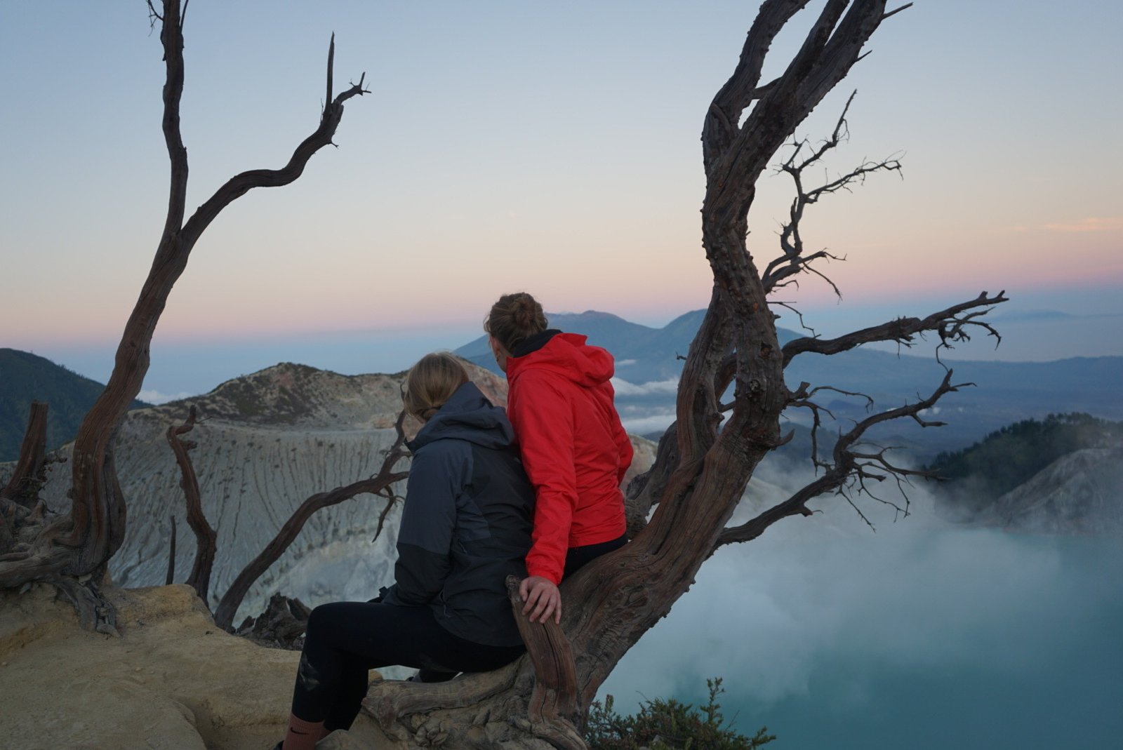 Two travelers overlooking the Ijen crater lake at dawn