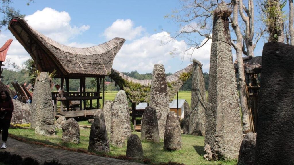 Traditional Torajan house and stone monuments in a green Sulawesi landscape
